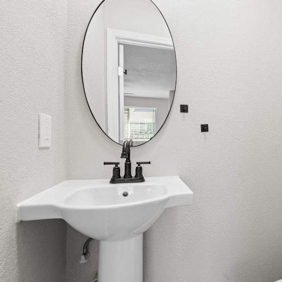 a white sink with a round mirror above it.