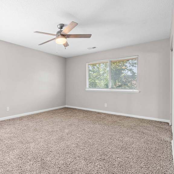 a room with a ceiling fan and two windows.