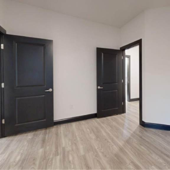 Thumbnail 4 of 10 A room with a black door and a wooden floor.