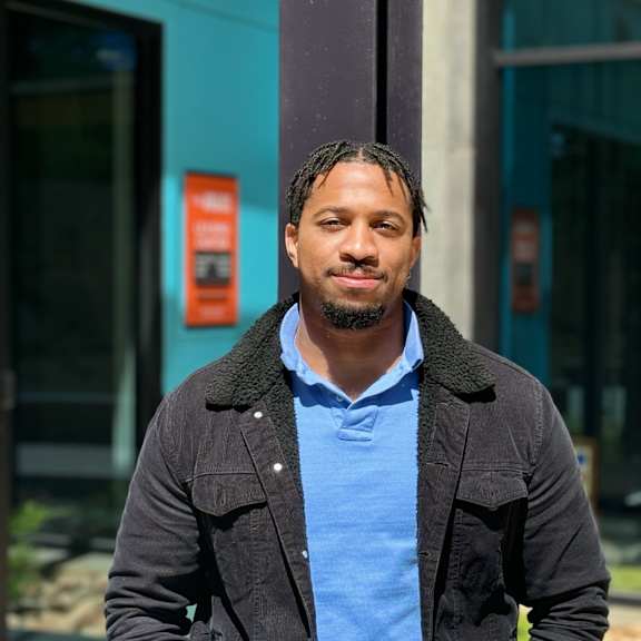 a man with a blue shirt and a black jacket is standing outside.