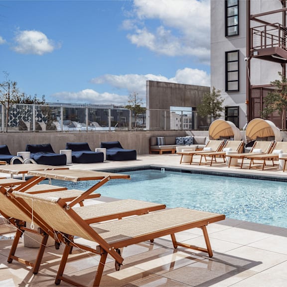 a pool with sun loungers and a building in the background.