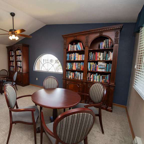 a room with a round table and chairs and a bookcase filled with books.
