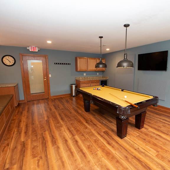 a pool table in a room with wood flooring and a clock on the wall.