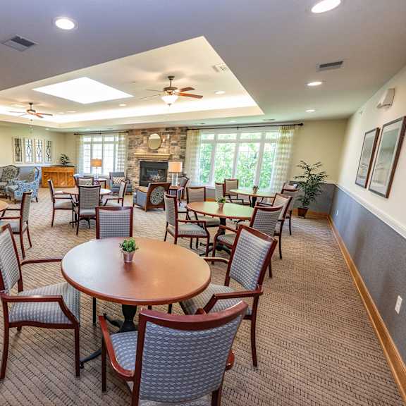 a large room with a table and chairs in the foreground and a fireplace in the background.