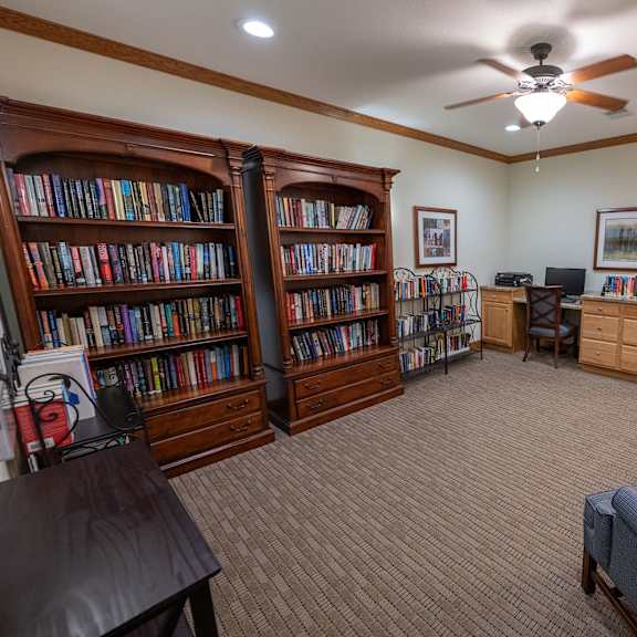 a room with a carpeted floor, a ceiling fan, and a bookshelf filled with books.