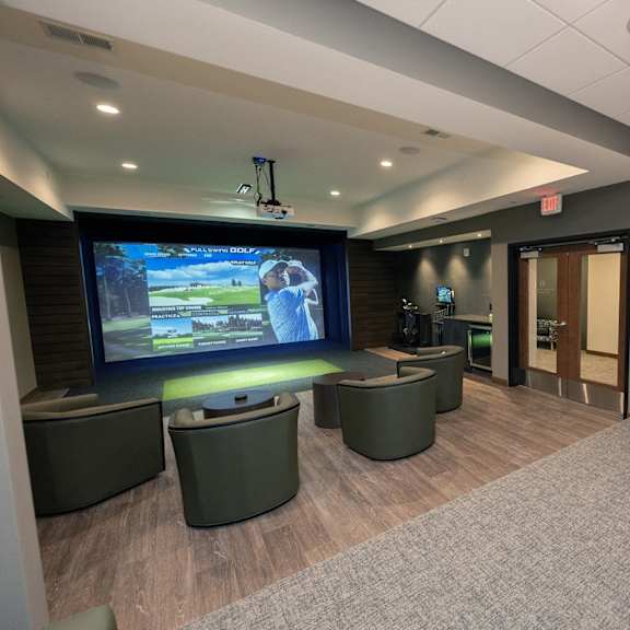 a golf-simulator room with a large screen and comfortable seating.
