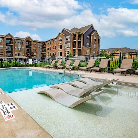 a swimming pool with lounge chairs in front of an apartment building