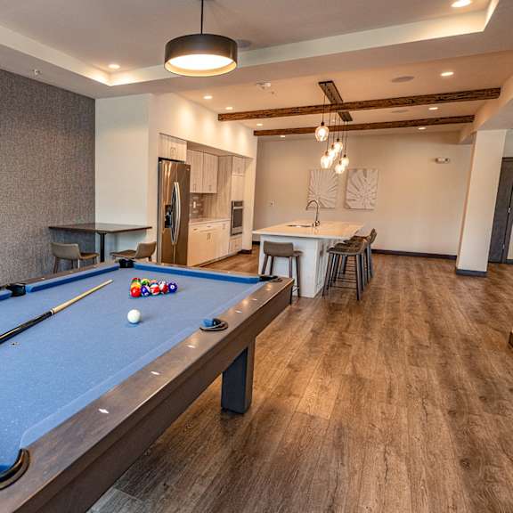 a pool table in a clubhouse with a bar and a kitchen