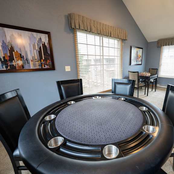 a black table with a round top and silver legs is surrounded by black chairs in a room with a painting on the wall.