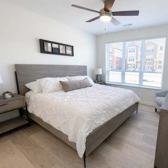 a bedroom with a large bed, a ceiling fan, and a window with a view of a building outside.