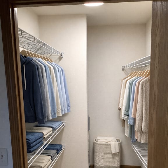 a small closet with clothes hanging on shelves and a basket on the floor.