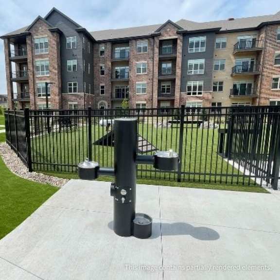a black metal fence surrounds a grassy area in front of a brick apartment building.