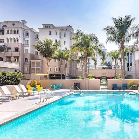 a swimming pool surrounded by palm trees and lounge chairs. at la jolla crossroads apartments, san diego