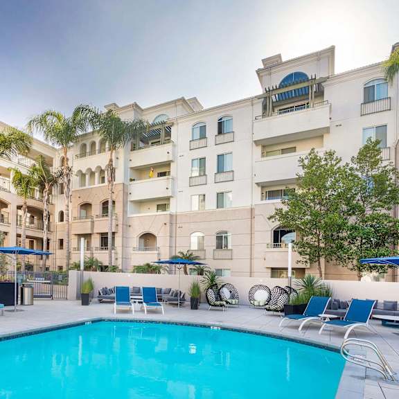 a swimming pool in front of a building with a blue umbrella. at la jolla crossroads apartments, san diego, 92122