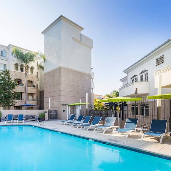 a pool surrounded by lounge chairs in front of a building. at la jolla crossroads apartments, san diego, ca, 92122