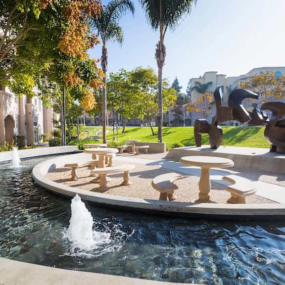 a fountain in the middle of a park with a sculpture in the background. at la jolla crossroads apartments, california