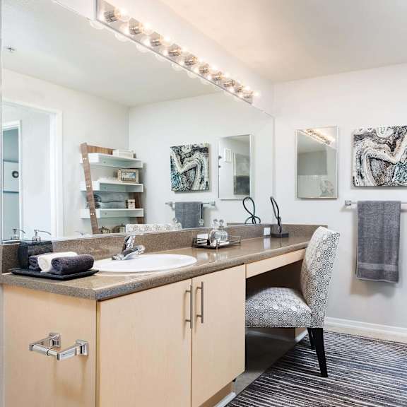 a bathroom with a vanity, a chair, and a mirror. at la jolla crossroads apartments, san diego, ca, 92122