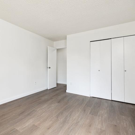 a room with white walls and wooden flooring with two white cupboards.