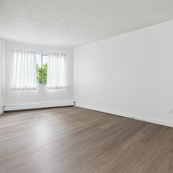 a room with wooden flooring and a window with white curtains.