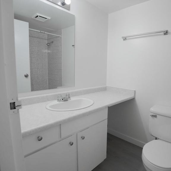 a white bathroom with a toilet, sink, and mirror.