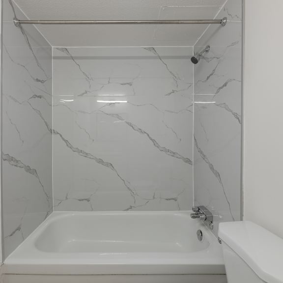 a white bathroom with a marble wall and a white tub.