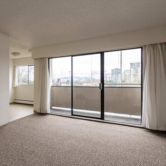 a room with a carpeted floor and a large window with a view of buildings outside.