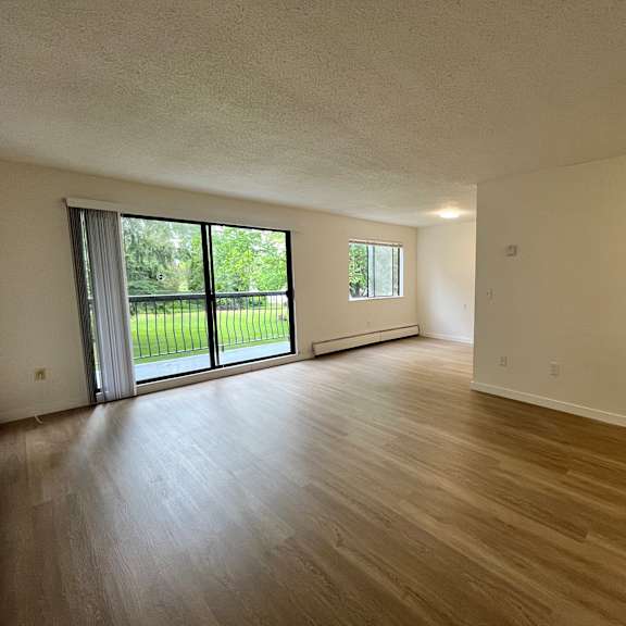 a room with wooden floors and white walls, featuring a sliding glass door.