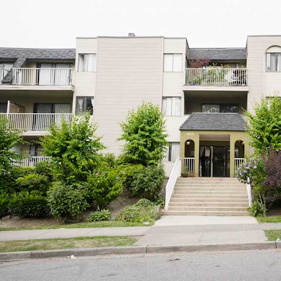 a building with a grey facade and a green lawn in front.