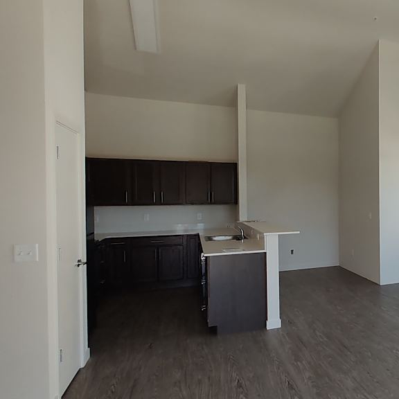 an empty living room with a kitchen in the background