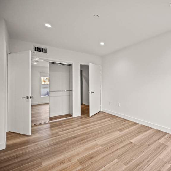 a room with wooden floors and white walls, with a door on the left and two open doors on the right.