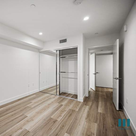 a room with white walls and wood flooring with a door on the right.