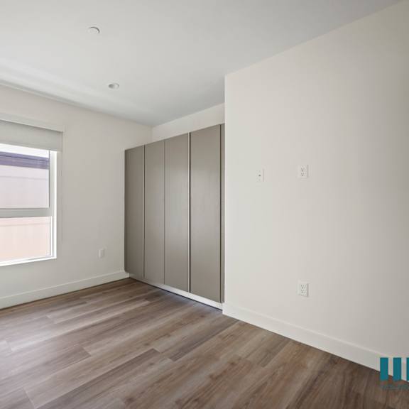 a bedroom with white walls and wood floors and a window