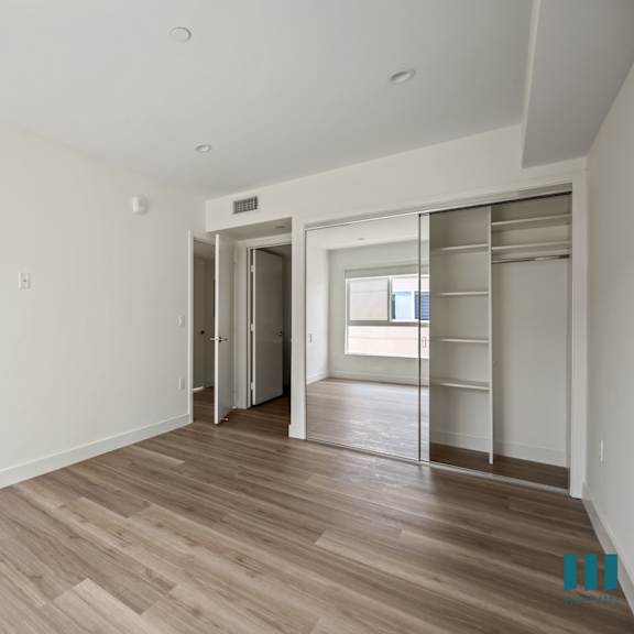 a bedroom with white walls and wood flooring and a closet