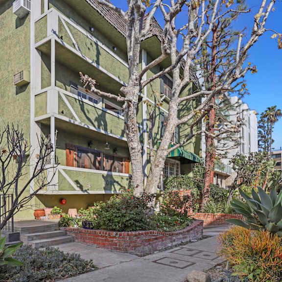 a green building with a balcony and a tree in front.