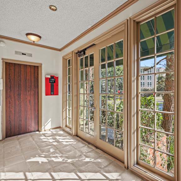 a hallway with a red door and a glass door with a view of trees outside.