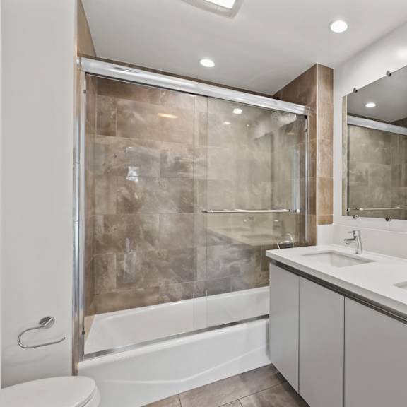 bathroom with shower bath with glass door, double-sink vanity with cabinet storage