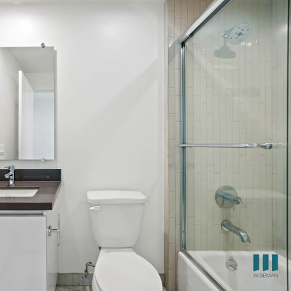 bathroom with full-size bathtub with glass door and vanity cabinet storage