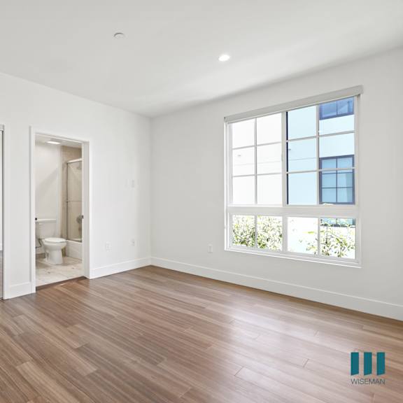 bedroom with bathroom, large closet with built-in shelving, windows, and vinyl flooring