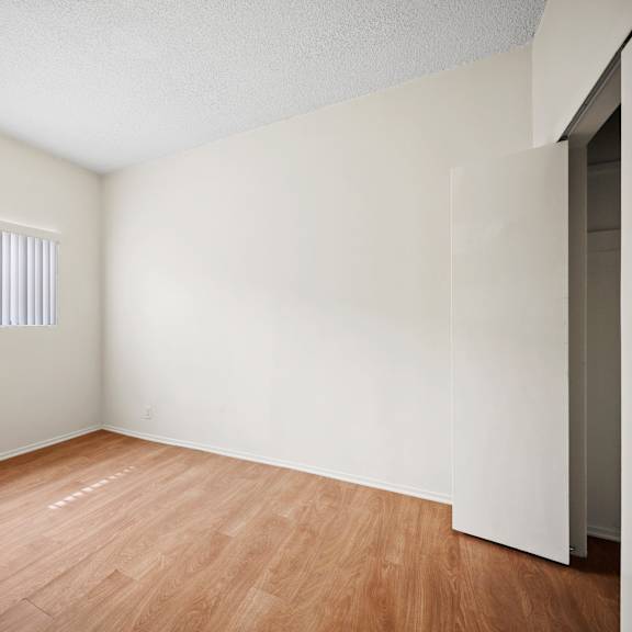the spacious living room of an apartment with wood flooring and a window