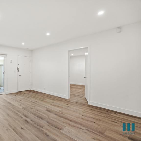 a spacious room with wooden flooring and white walls.