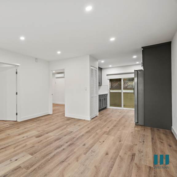 a spacious room with wooden flooring and white walls.