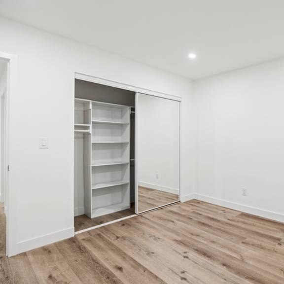 a white room with a wooden floor and a refrigerator in the corner.