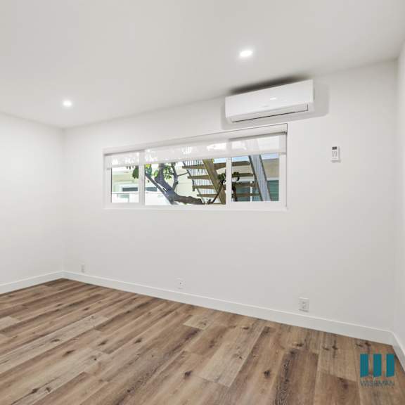 a room with wooden flooring and a window showing an outdoor tree.