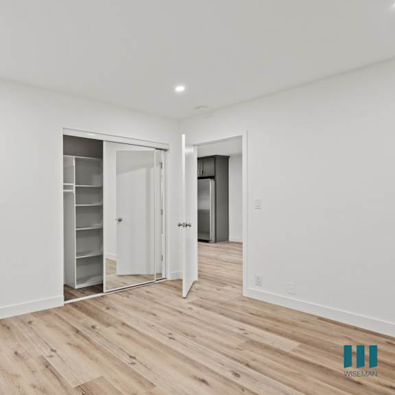 a spacious room with white walls and wooden flooring, featuring a walk-in closet with shelves and a mirror.