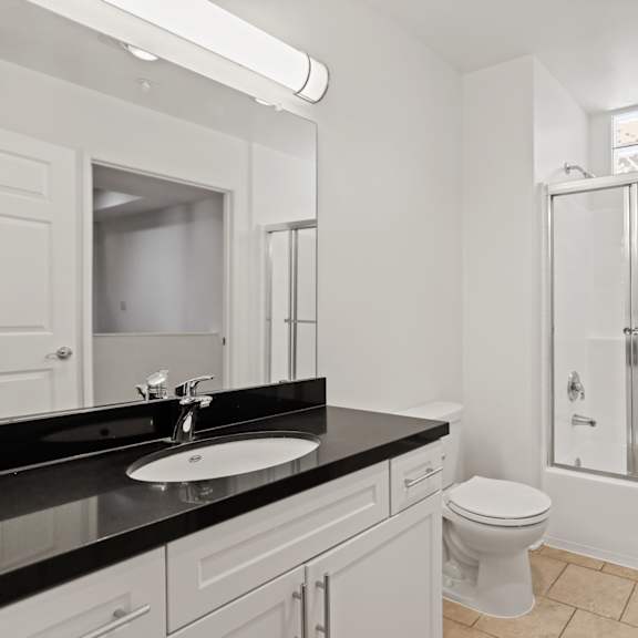 bathroom with full-size bathtub with glass door and vanity cabinet with storage