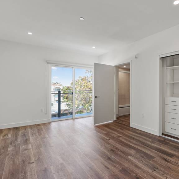 bedroom with vinyl flooring, large closet with built-in organizers, bathroom, and patio