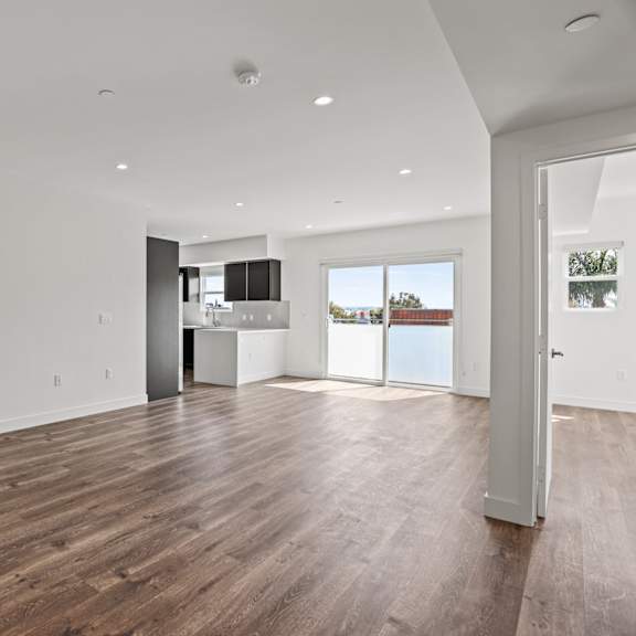 a living room and kitchen in a house with white walls and a wooden floor