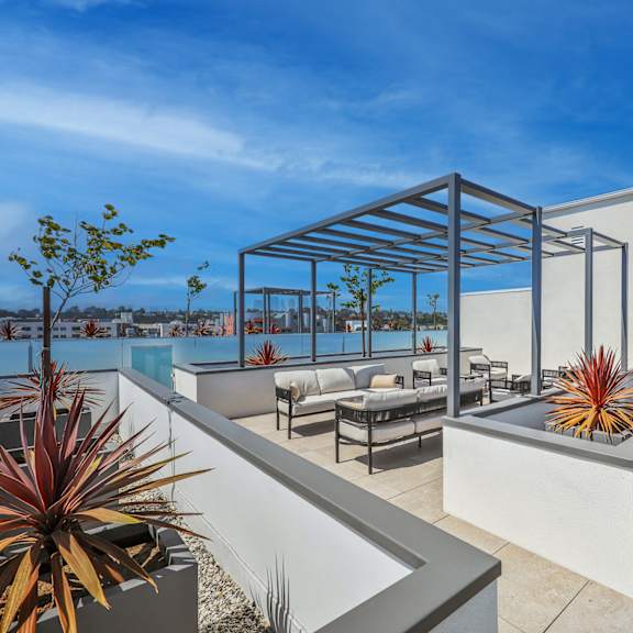 a modern outdoor patio area with a white wall, a couch, and a table.