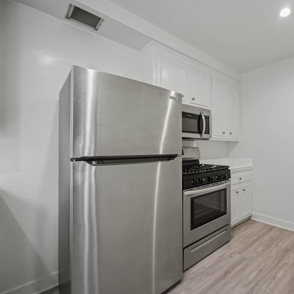 a modern kitchen with a stainless steel refrigerator, microwave, oven, and wooden flooring.