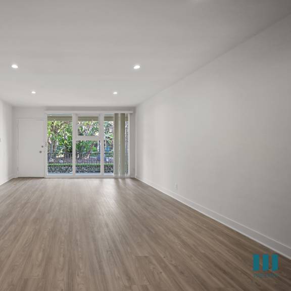 a spacious room with wooden flooring and a window with a view of greenery outside.